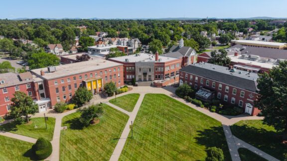 Aerial view of a college campus with red brick buildings around a green lawn and intersecting walkways leading to a central entrance.