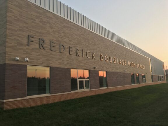 Exterior of Frederick Douglass High School: brick wall façade with large letters spelling the name, at sunset.